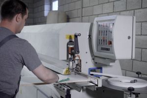 master is using industrial machine for processing edges of particle board in workshop of furniture plant, covering by plastic